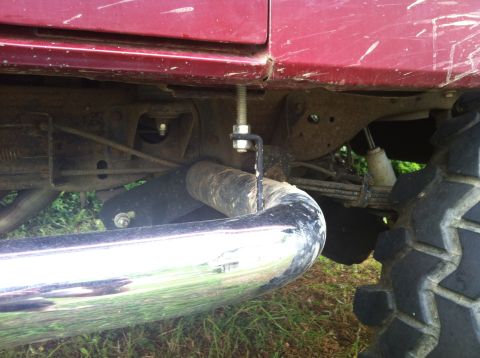 1991 Ford Bronco - Close-up view of the undercarriage of a red vehicle, a chrome exhaust pipe and a large off-road tire.