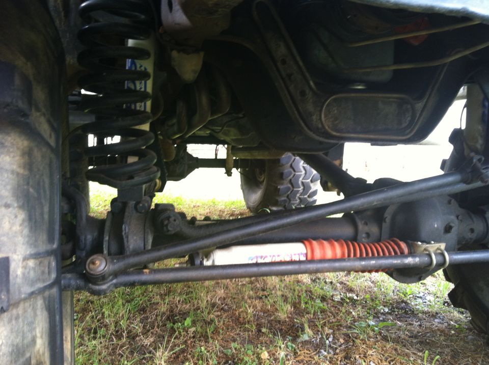 Undercarriage of a vehicle with large tires, showing suspension and steering components, with a "SUPERMOTORS" watermark