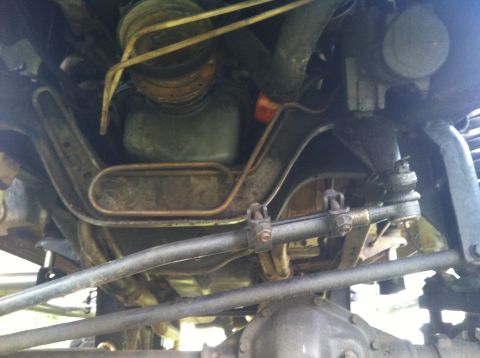 1991 Ford Bronco - The photo shows the underside of a vehicle, focusing on the steering and suspension system with various metal parts and hoses visible.
