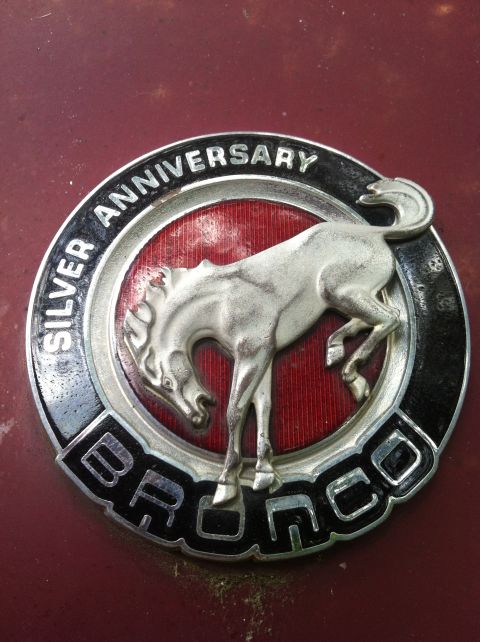 1991 Ford Bronco - A close-up of a Bronco Silver Anniversary badge is shown on a red surface.