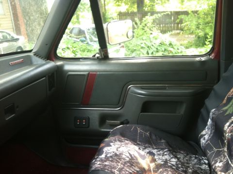 1991 Ford Bronco - The interior of a Ford Bronco shows a camouflage seat cover and a view of trees and a fence through the window.