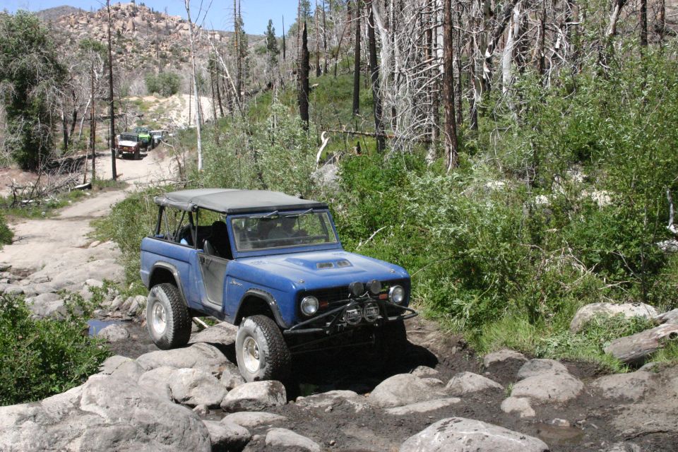 Blue first-gen Ford Bronco navigating a rocky trail with other vehicles behind it