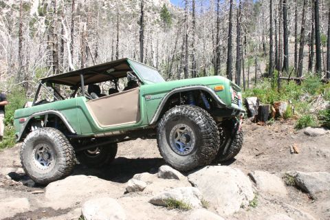 1991 Ford Bronco - This heavily modified green Bronco navigates a rocky trail with its top removed and suspension lifted.
