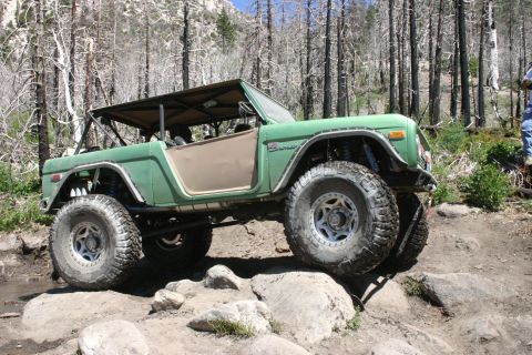 1991 Ford Bronco - Modified green Ford Bronco navigating a rocky trail in a wooded area.