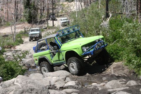 1991 Ford Bronco - A modified Ford Bronco tackles a rocky off-road trail with other vehicles following.