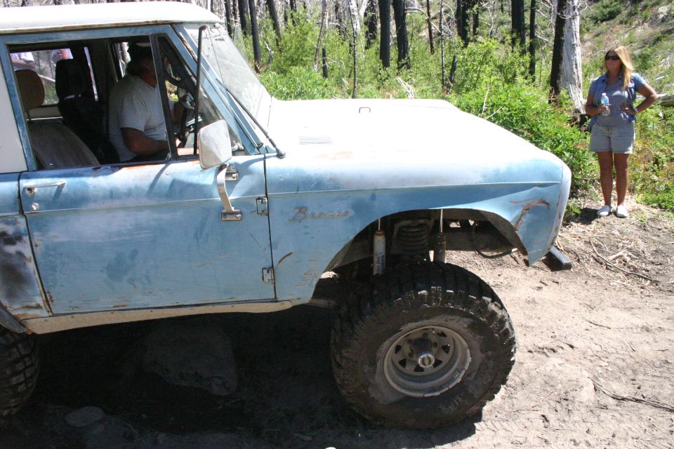 Light blue Ford Bronco with a white roof, lifted suspension, and off-road tires, parked on a dirt road