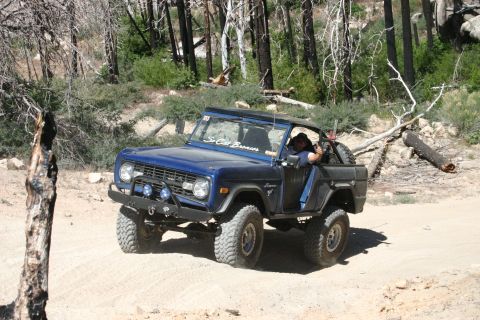 1991 Ford Bronco - A blue first-generation Ford Bronco navigates a dirt road through a forest.