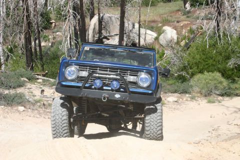 1991 Ford Bronco - A blue Ford Bronco navigates a dirt path surrounded by trees and rocky terrain.