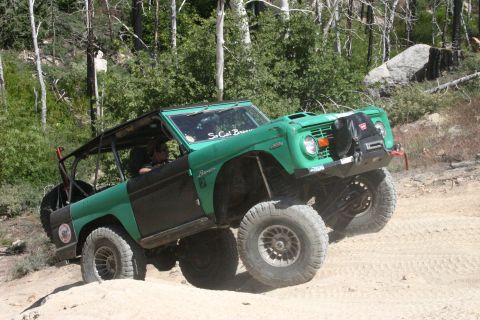 1991 Ford Bronco - This modified Ford Bronco is navigating a steep, sandy incline in a wooded area.