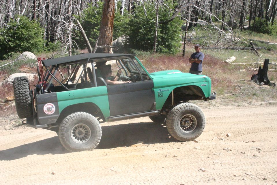 Green and black Ford Bronco with a soft top and spare tire on the back, driving on a dirt road