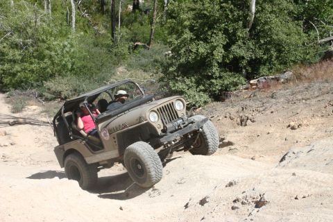 1991 Ford Bronco - A tan Jeep CJ-5 navigates a challenging off-road trail with two occupants visible.