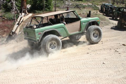 1991 Ford Bronco - A modified green Ford Bronco navigates a dusty trail with other vehicles in the background.