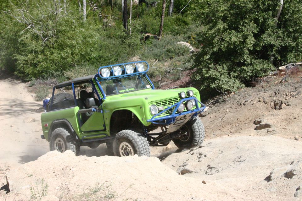 Green Ford Bronco with blue roll cage and lights driving on a dirt trail