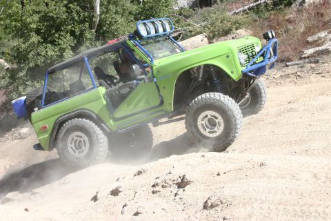 1991 Ford Bronco - This heavily modified SUV is kicking up dust as it navigates a steep, sandy incline.
