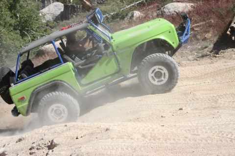 1991 Ford Bronco - Modified green off-road vehicle navigates a dusty, rocky terrain.