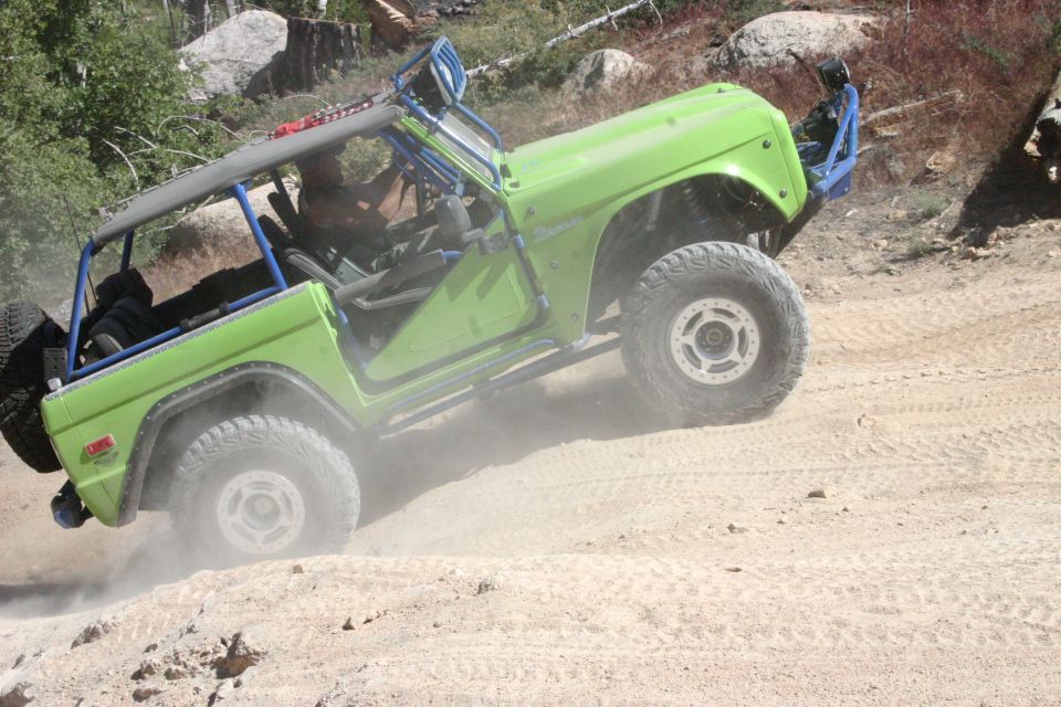 Green off-road vehicle with roll cage on a dirt hill, kicking up dust