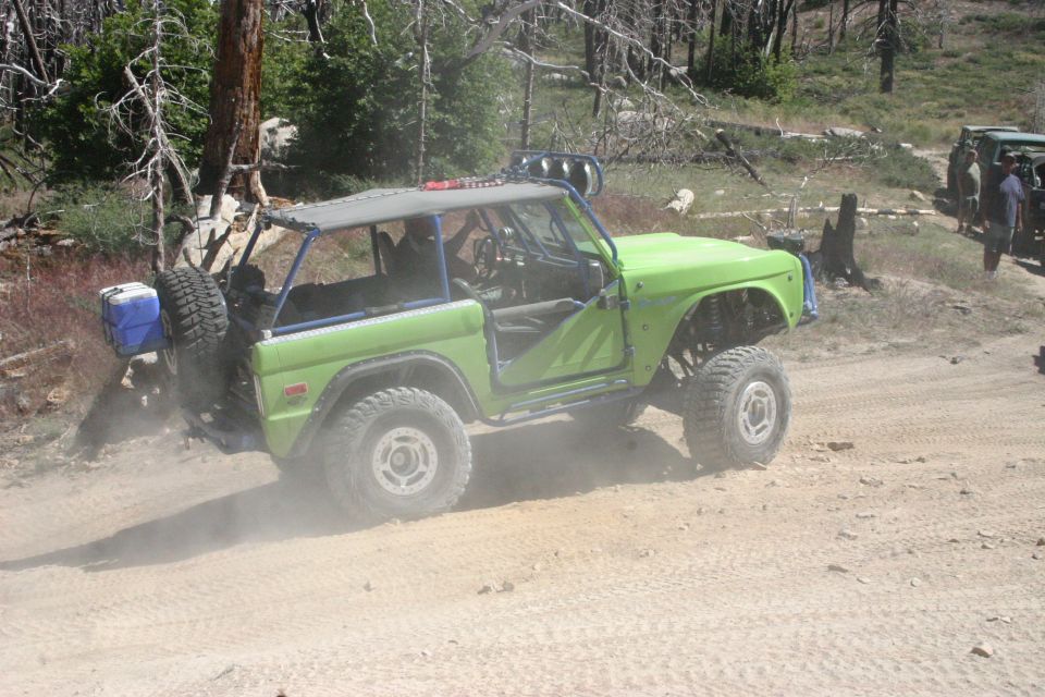 Green off-road Bronco with roll cage on dirt road