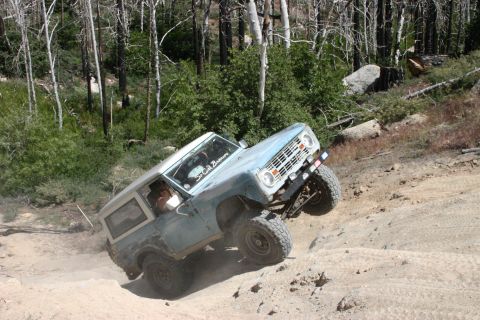 1991 Ford Bronco - Early 1970s Ford Bronco tackles a steep, rocky off-road trail in a wooded area.