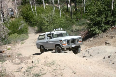 1991 Ford Bronco - This Ford Bronco is navigating a challenging off-road trail in a wooded area.