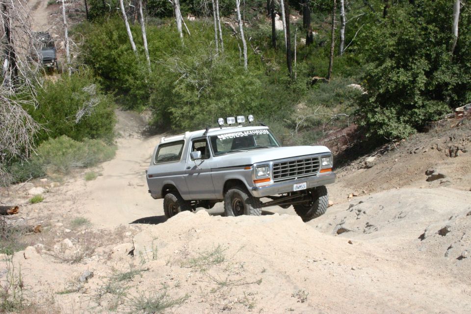 Silver Ford Bronco driving on a dirt trail with another vehicle behind it