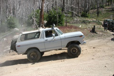 1991 Ford Bronco - This lifted white Ford Bronco is navigating a dusty, wooded trail, with another vehicle visible in the background.