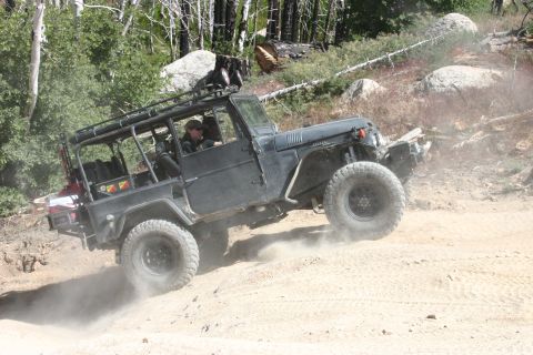 1991 Ford Bronco - A dark-colored off-road vehicle navigates a dusty trail in a wooded, rocky area.