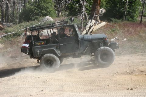 1991 Ford Bronco - This dark-colored off-road vehicle is seen navigating a dusty trail, equipped with a prominent roof rack and large tires.