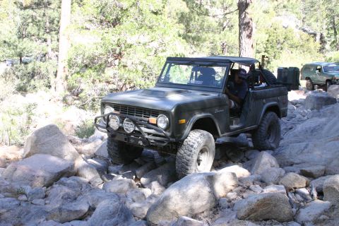 1991 Ford Bronco - This classic Ford Bronco navigates a challenging rocky trail, with another SUV visible in the background.