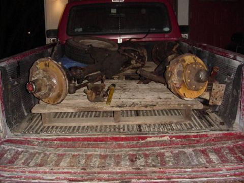 1992 Ford Bronco - Various used vehicle parts are piled in the bed of a red pickup truck.
