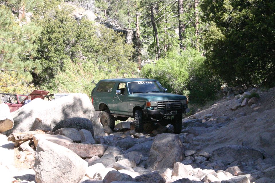 Green SUV navigating rocky terrain, "ABUSED" sticker on windshield