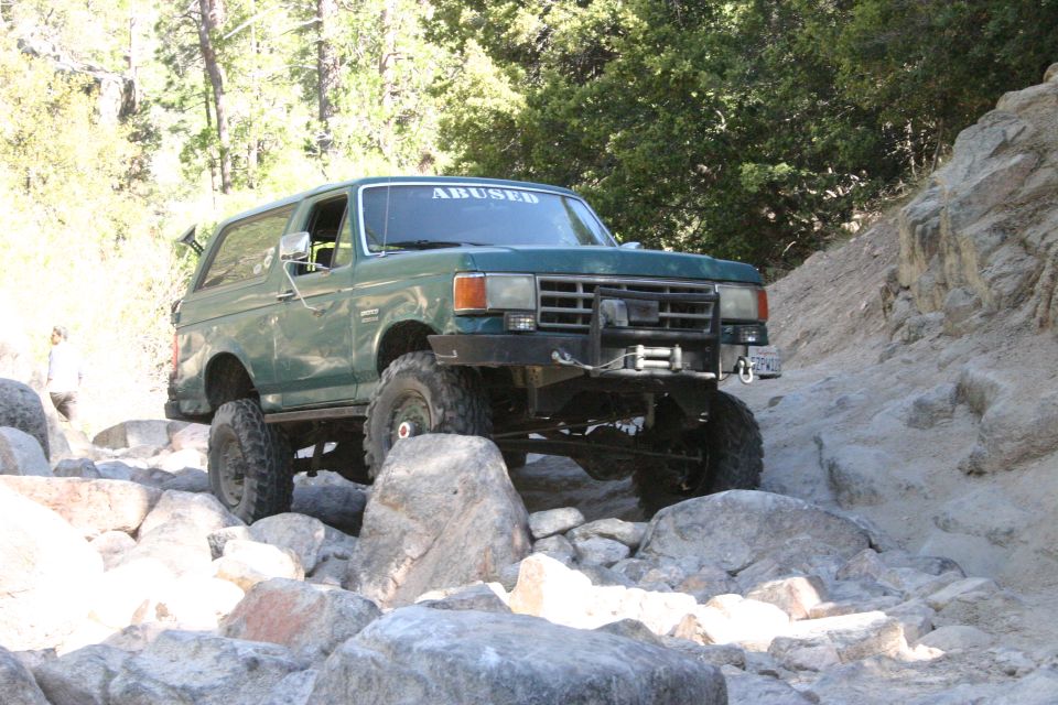 Green Ford Bronco with "ABUSED" on windshield driving over rocks on a trail