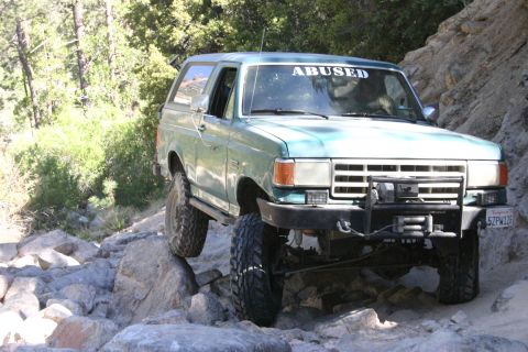 1991 Ford Bronco - This modified Ford Bronco navigates a rocky trail, its "ABUSED" windshield sticker hinting at its off-road adventures.