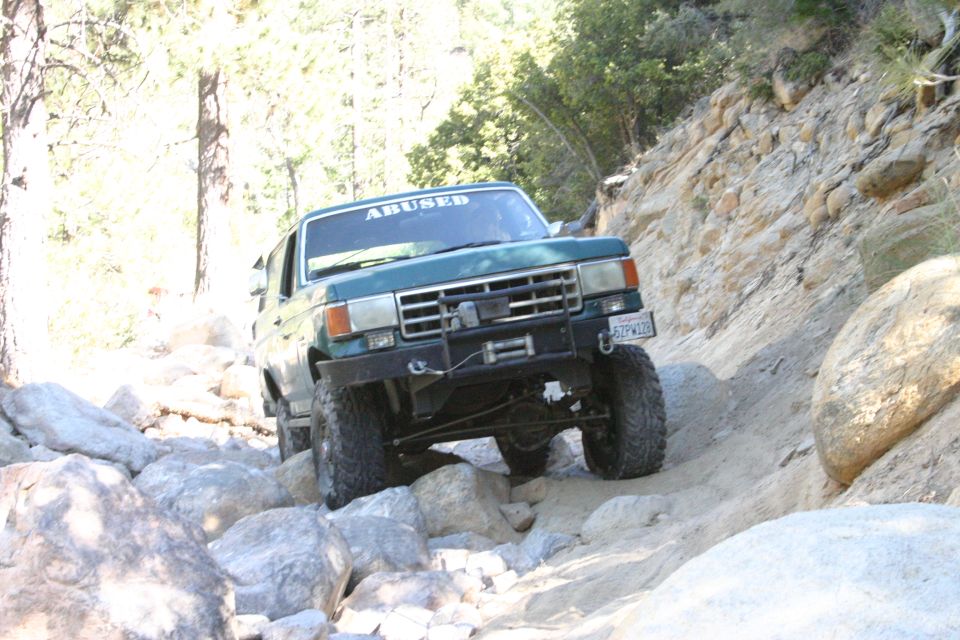 Green Ford Bronco with a winch and off-road tires navigating a rocky trail