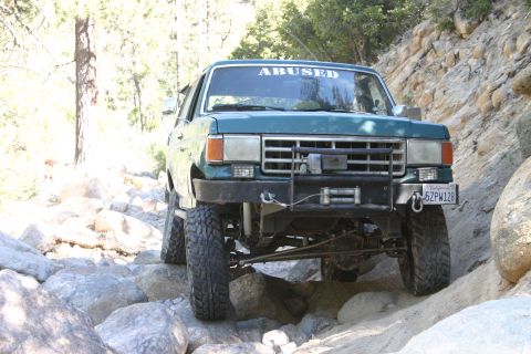 1991 Ford Bronco - This modified 1991 Ford Bronco navigates a challenging rocky trail, displaying an "ABUSED" banner on its windshield.