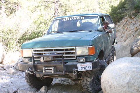 1991 Ford Bronco - Green 1991 Ford Bronco tackling a challenging off-road trail with a driver visible.