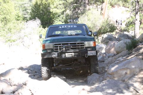 1991 Ford Bronco - This modified Ford Bronco navigates a challenging, rocky trail with trees and boulders visible.
