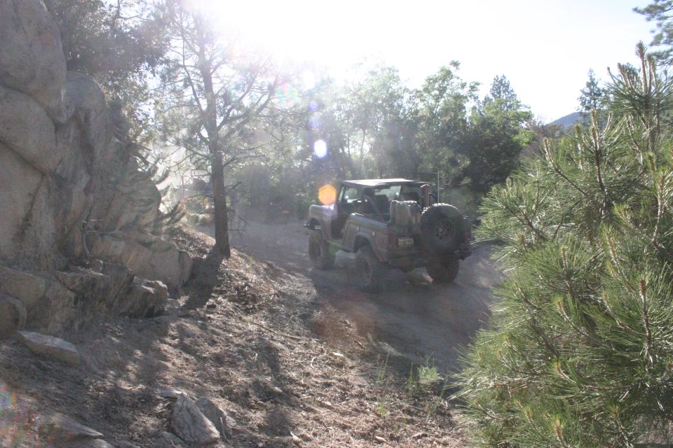 off-road vehicle driving up a dusty trail with rocks and trees