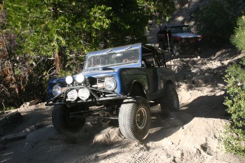 1991 Ford Bronco - Two off-road vehicles navigate a steep, rocky path through a wooded area.