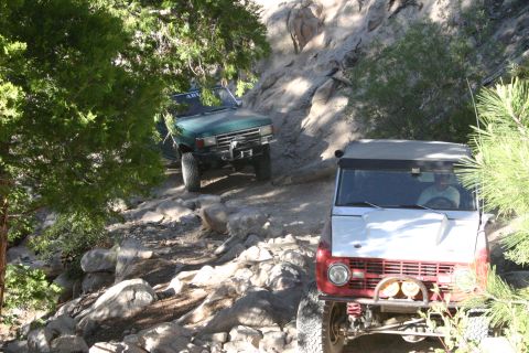1991 Ford Bronco - Two 4x4 vehicles tackle a challenging rocky path on an off-road trail.