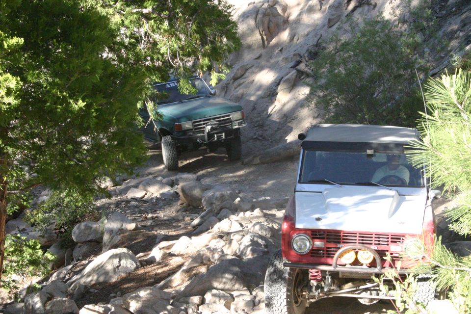 Two off-road vehicles navigating a rocky trail, one red and white in the foreground, a green one behind it