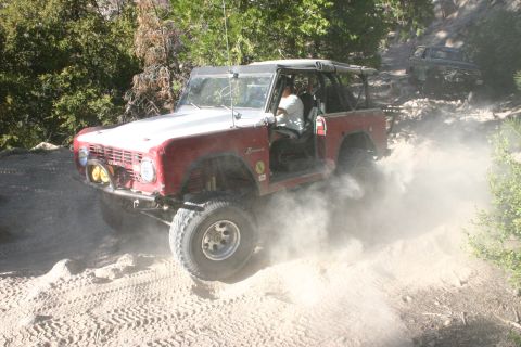 1991 Ford Bronco - A red and white Ford Bronco navigates a dusty off-road trail, with a second vehicle following closely.