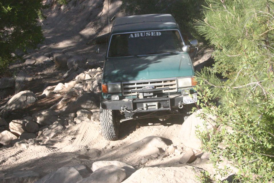1991 Ford Bronco navigating a rocky trail, windshield banner reads 'ABUSED'. License plate 5ZPW128