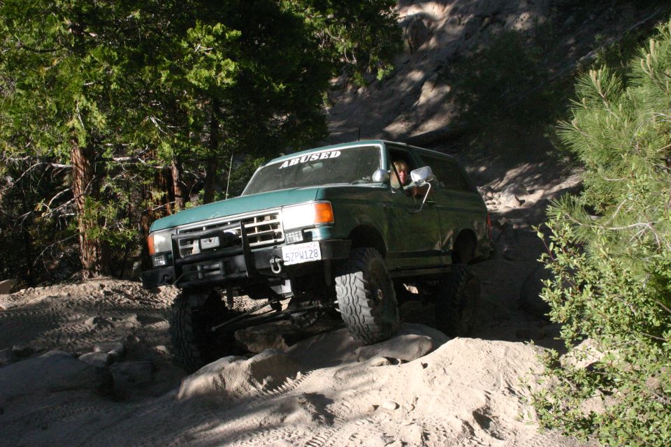 Green Ford Bronco off-roading on a rocky trail, front bumper and grille visible