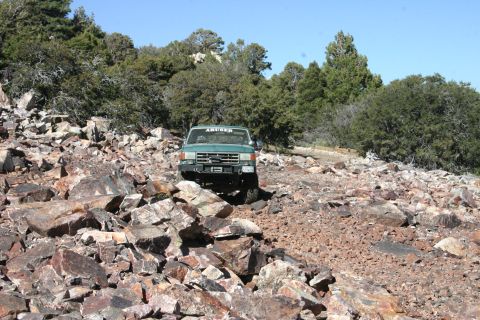1991 Ford Bronco - A green truck navigates a rocky trail under a clear blue sky.