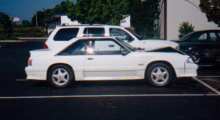 1982 Ford Bronco - A white 1987 Ford Mustang GT coupe is parked in a lot with its hood open, alongside other vehicles.