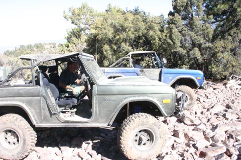 1991 Ford Bronco - Two Ford Broncos navigate a rocky, off-road trail under a clear sky.