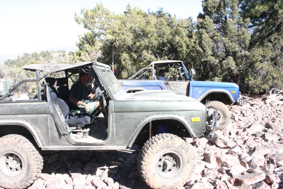 Two Ford Broncos on a rocky trail, one green and one blue. The green Bronco is in the foreground with a driver