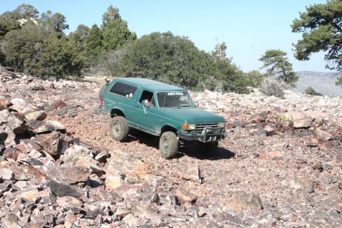 1991 Ford Bronco - A green SUV navigates a rocky, off-road path under a clear blue sky.
