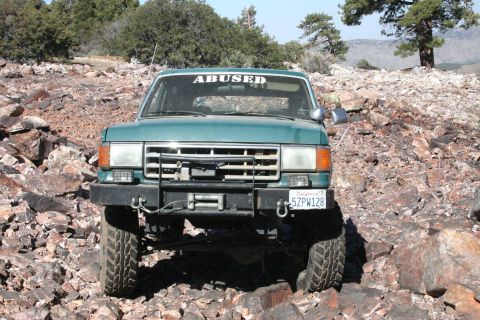 1991 Ford Bronco - Off-road SUV navigates a rocky trail, displaying a custom windshield decal.
