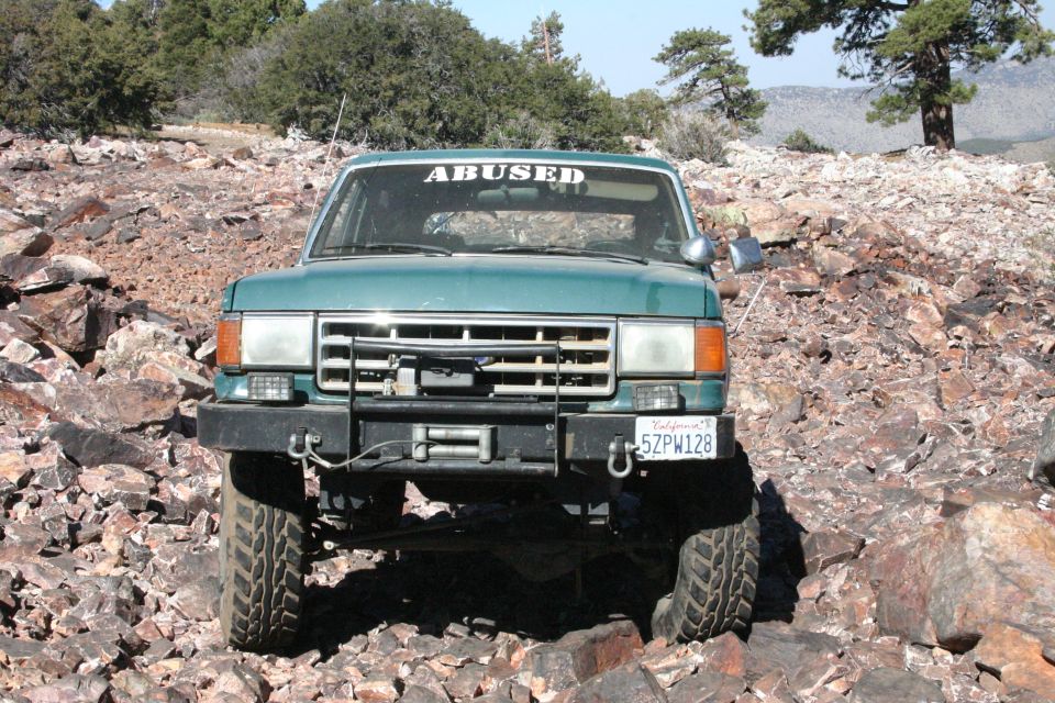 Green SUV with 'ABUSED' sticker on windshield, driving over rocks. License plate 5ZPW128
